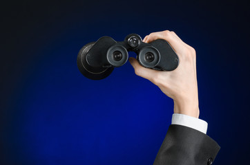 Business and search topic: Man in black suit holding a black binoculars in hand on a dark blue background in studio isolated