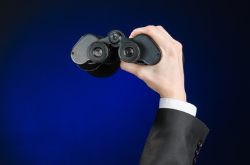 Business and search topic: Man in black suit holding a black binoculars in hand on a dark blue background in studio isolated