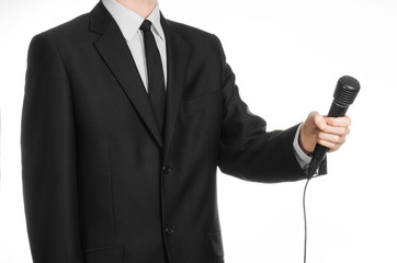Naklejka premium Business and speech topic: Man in black suit holding a black microphone isolated on white background in studio
