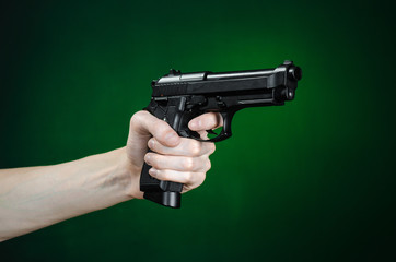 Firearms and murderer topic: human hand holding a gun on a dark green background isolated in studio