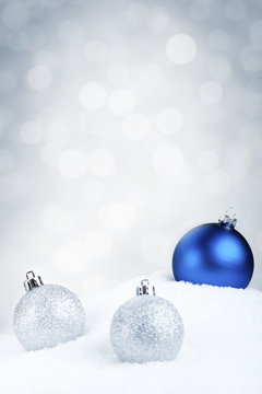 Blue and silver Christmas baubles on snow, silver background