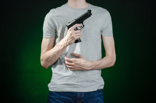 Firearms and murderer topic: man in a gray t-shirt holding a gun on a dark green background isolated in studio