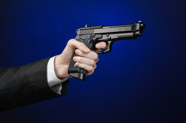 Firearms and security topic: a man in a black suit holding a gun on a dark blue background in studio isolated