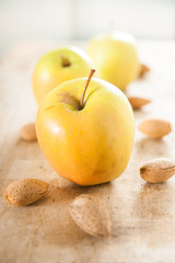 Three golden delicious apples with almonds in shells on rustic wood