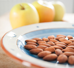 Toasted almonds on terra cotta painted dish with three golden delicious apples on the background