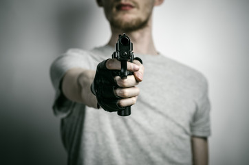 Horror and firearms topic: the killer with a gun in his hand in black gloves on a gray background...