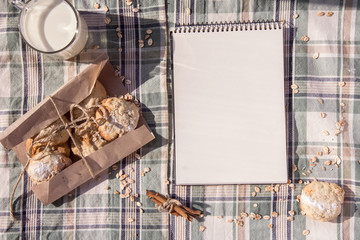 Pure notebook, a glass of milk, oat cookies in a paper, tablecloth