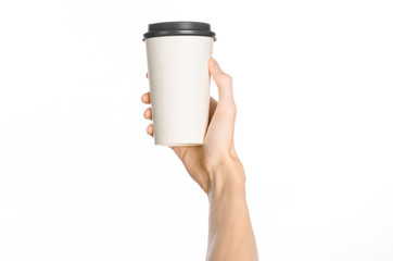 Breakfast and coffee theme: man's hand holding white empty paper coffee cup with a brown plastic cap isolated on a white background in the studio, advertising of coffee first-person view