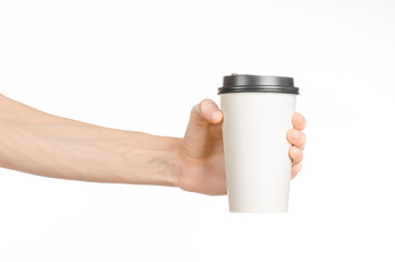 Breakfast and coffee theme: man's hand holding white empty paper coffee cup with a brown plastic cap isolated on a white background in the studio, advertising coffee