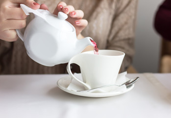 Woman pours tea from white teapot in a white cup
