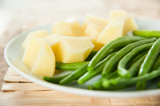 Cooked potatoes and green beans on white ceramic dish on table mat