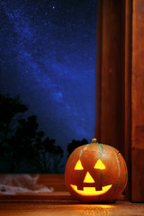 Halloween pumpkin head jack o lantern near window, night sky full of stars on background