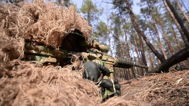 Close-up of aiming sniper/Sniper in camouflage suit ghillie aiming from his rifle in forest