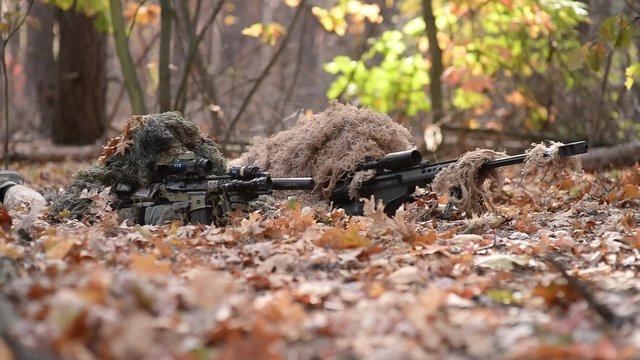 Team of snipers in forest on fire position/Two armed men with rifles with optical sights in ghillie suit in autumn forest