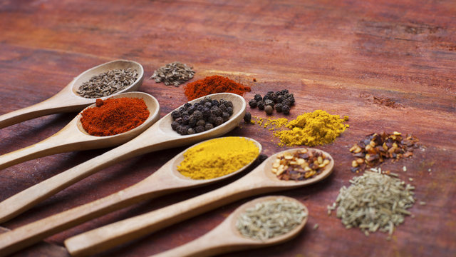 Wooden spoons full of aromatic herbs and spices on a wooden cutting board