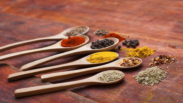 Wooden spoons full of aromatic herbs and spices on a wooden cutting board