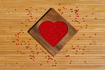 Heart from red beads in wooden heart-shaped box on the background of bamboo
