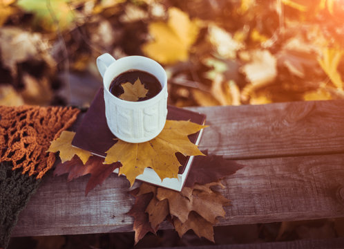 Hot coffee and book with autumn leaves on wood background