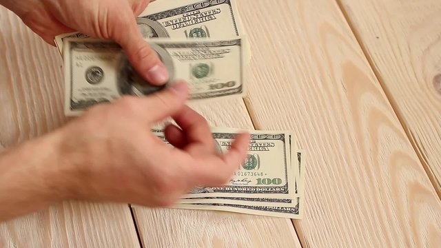 human hands recalculate a large sum of one hundred dollar bills on a wooden background