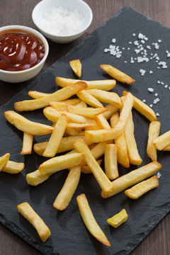 French fries, tomato sauce and salt on a blackboard, top view