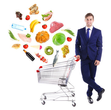 Young Man Pushing Shopping Cart With Different Food, Isolated On White