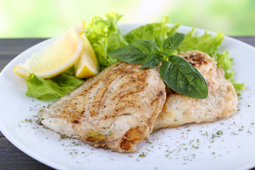 Dish of fish fillet with greens and lemon on table close up