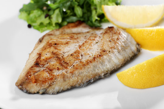 Dish of fish fillet with greens and lemon on plate close up