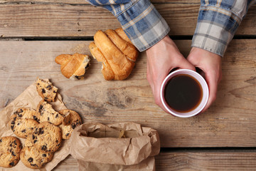 Female hands holding cup of coffee and cookies on wooden table close up