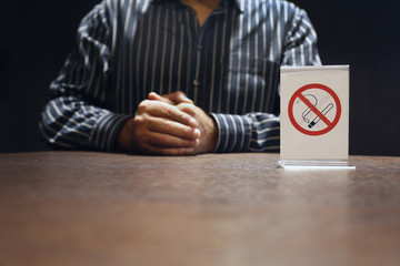 Man holding hands near plastic No smoking symbol on wooden table