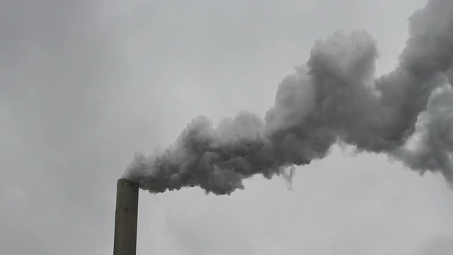 Thick smoke flowing out of a high factory chimney on a stormy day.