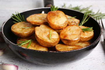 Delicious baked potato with rosemary in frying pan on table close up