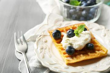 Sweet homemade waffles on plate, on color wooden background