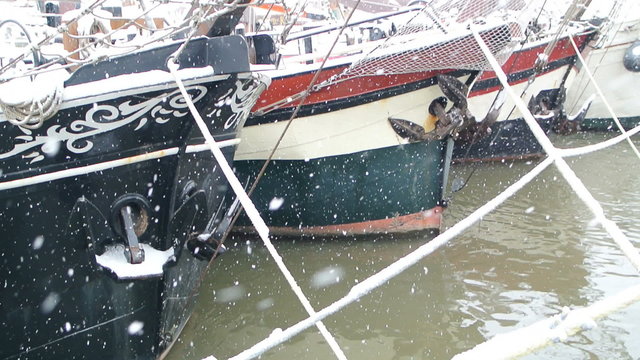Snow falling down on classic sailing ships docked on the quays of the city of Kampen.