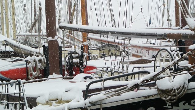 Snow falling down on classic sailing ships docked on the quays of the city of Kampen.