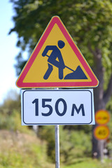 Road signs "Roadwork", "Distance of 150 m" against greens