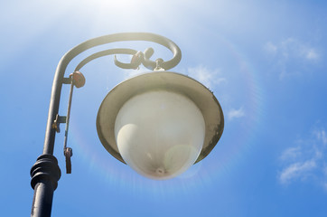 Old street lamp on a background of blue sky with clouds. Backlight. Highlights sun.