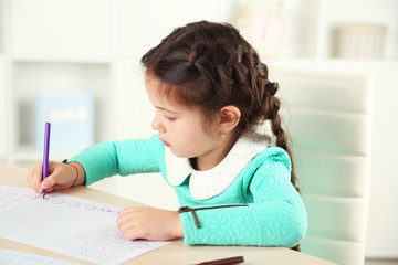 Naklejka na ściany i meble Cute little girl doing her homework, close-up, on home interior background