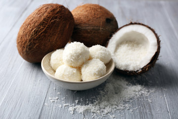 Candies in coconut flakes and fresh coconut on color wooden background