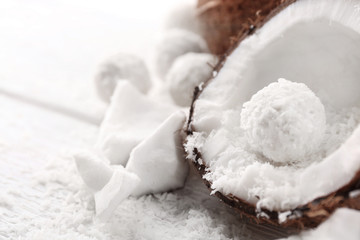 Candies in coconut flakes and fresh coconut on  light wooden background