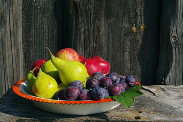 Plums, pear and apple in the iron bowl on a wooden background. Fresh autumn crop of fruit.