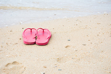 Fototapeta na wymiar Red old slippers and flower on the beach background
