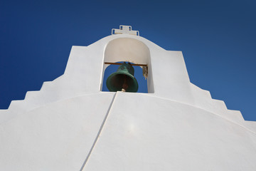 Architectonic detail of a small white church with a bell and a cross in Milos island