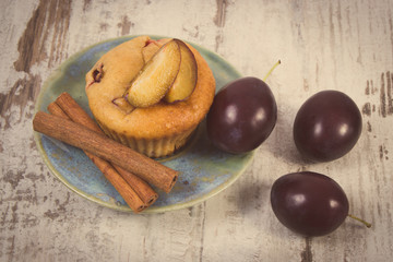 Vintage photo, Fresh baked muffins with plums and cinnamon sticks on old wooden background, delicious dessert