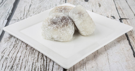 Japanese confection, round glutinous rice stuffed with sweetened red bean paste or locally known as daifukumochi in a white plate over wooden background