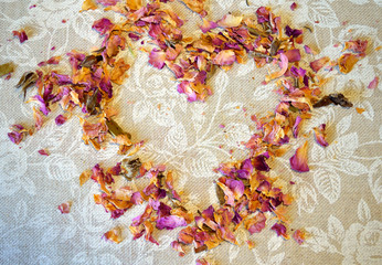 Heart of dried petals of tea rose on tablecloth with white roses and place for your text
