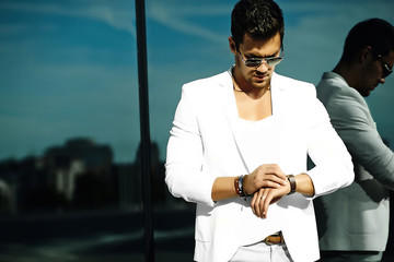 Fashion portrait of young sexy handsome model man in casual white suit in sunglasses in white suit in the street