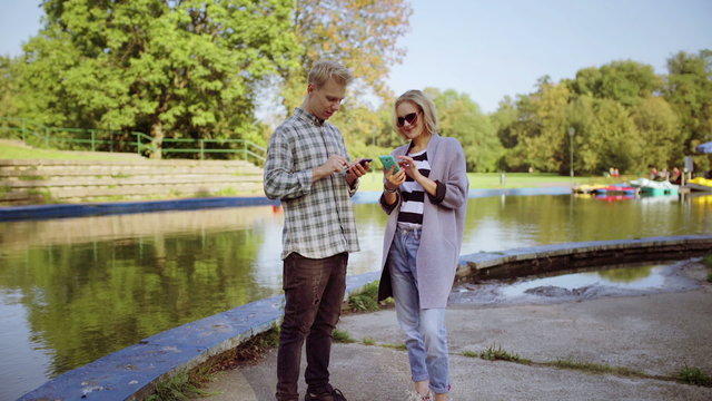 Couple standing next to the river and using smartphones

