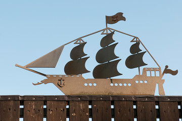 Antique ship silhouetted against a blue sky on garden fence.