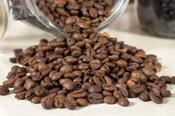 Roasted coffee beans get out of an overturned and open glass jar