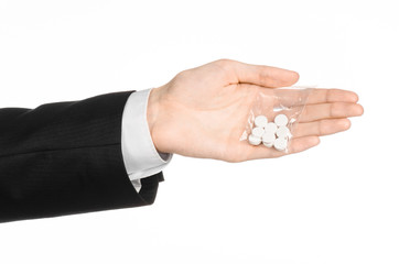 Fototapeta premium Addiction and business topic: hand in a black suit holds bag with white pills a drug on a white isolated background in studio